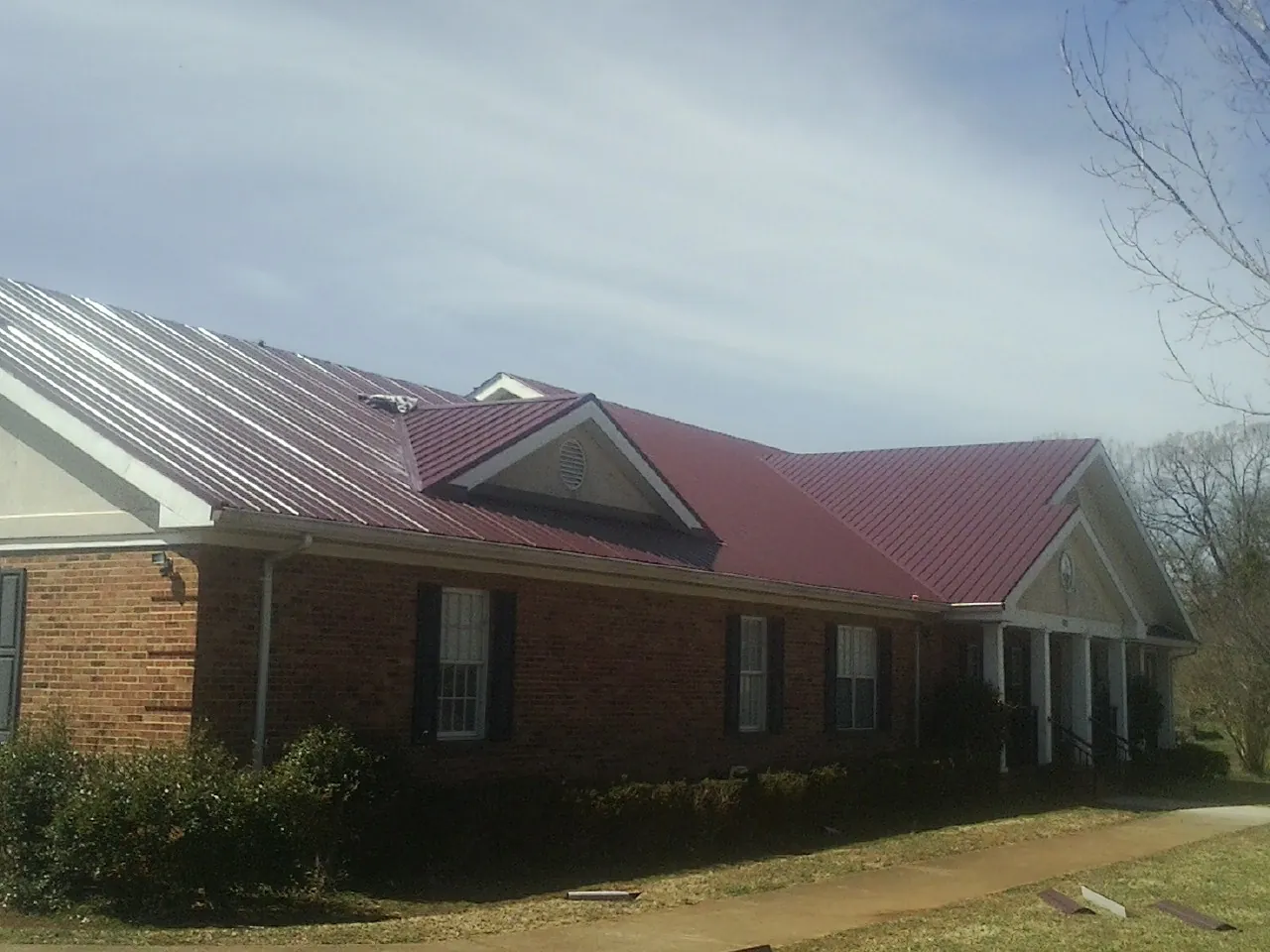 Red metal roof with gabled entries on a long brick building, from a Hail Damage Roof Repair job in Lafitte