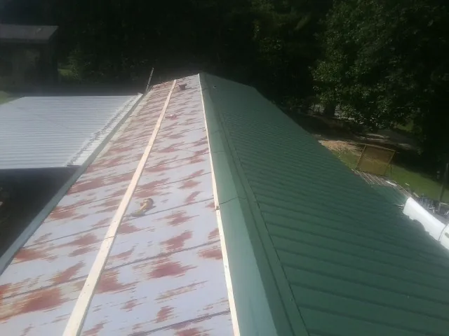 Old rusted panels beside newly installed green metal roofing — Wind Damage Roof Repair by Roofing Brothers in Lafitte