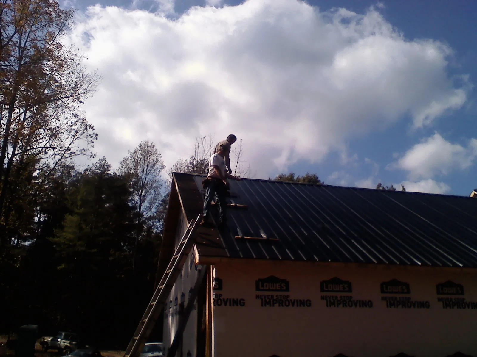 Roofer fastening dark metal panels high against a cloudy sky, from a Roof Inspection job in Lafitte
